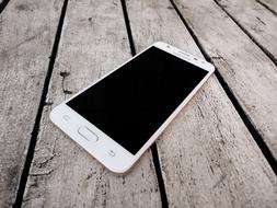 White mobile phone with black screen on the wooden surface