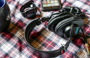 Beautiful, black headphones, blue and black cup, black smartwatch and black Iphone on the beautiful and colorful, checkered cloth