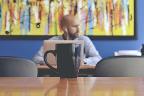 Beautiful, black cup on the wooden table, near the man, working with the laptop, near the colorful painting