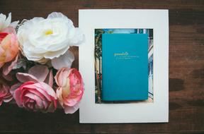Blue diary in a white frame and a bouquet of beautiful and colorful flowers on a wooden table
