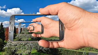 Person holding Samsung Galaxy S4 smartphone, on the beautiful, colorful landscape under the blue sky with white clouds