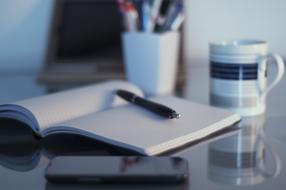a pen on a notebook and a cup of coffee on a desktop