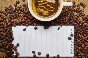 a cup of coffee, scattered coffee beans and a notebook on the table