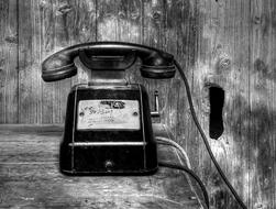 Black and white photo of the beautiful, black, retro phone at background with the wooden wall