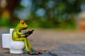 toy Frog with Mobile Phone sits on Toilet