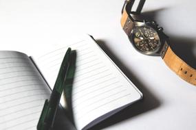 pen on notepad and men's wrist watch