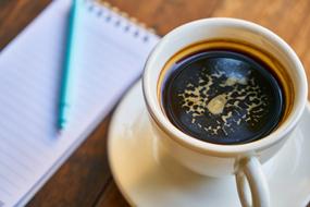 a cup of espresso and a notebook with a pen on the table