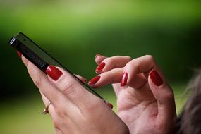 Woman with red nails, wearing ring, using smartphone