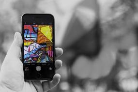 Black and white photo with the Iphone, with colorful graffities on the screen, in the hand