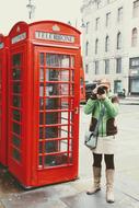 tourist with a camera near a red booth in london