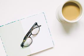 Cup of coffee, near the notebook with the eyeglasses, in light and shadow