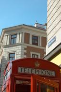 Beautiful, retro, red telephone booth, among the buildings in London, England, at blue sky on background