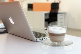 a cup of delicious cappuccino and a macbook on the table