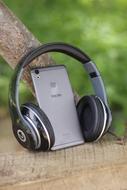 Beautiful headphones and gray smartphone, on the wood, among the green grass