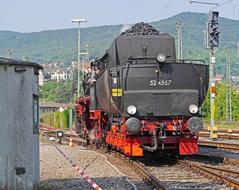 Black and orange br52 steam locomotive on the railway, among the green plants, at beautiful city on background