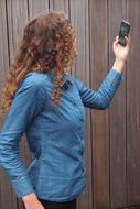 Woman with curly hair, making selfie on the smartphone, near the wooden wall