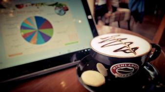 a cup of cappuccino with foam in front of the tablet screen