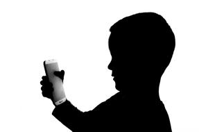 Black silhouette with the profile portrait of a kid, using smartphone at white background