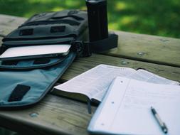 Bible, notebook with the pen, near the bag with the laptop, on the wooden surface, near the green plants