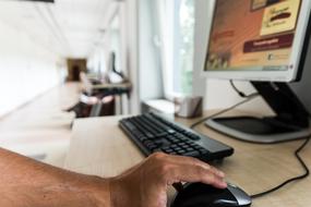 Male hand on a black and grey mouse at computer with black keyboard