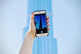 Female, taking a photo of the beautiful building, at blue sky on background, with the cell phone