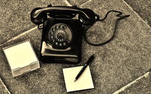 Retro photo of the old, beautiful, black phone, near the notes and pen