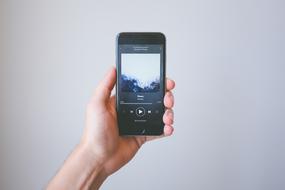 Person, listening to music, on the smartphone, in the hand, at white wall on backgorund