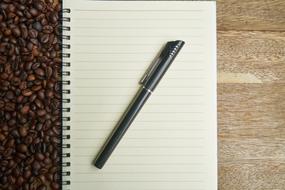 Black pen on the beautiful notebook among the coffee beans and wooden surface