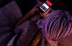 dark skin girl with purple dreads looking at smartphone