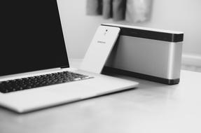 black and white photo of a laptop with a smartphone on the desk