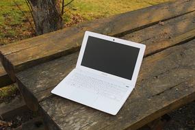 white laptop on wooden park bench