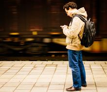 a man with a smartphone stands on a railway platform