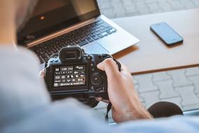 Person, using the camera at the workspace, with the laptop and smartphone on the wooden table