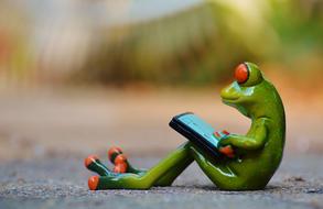 Figure of the cute, yellow, green and orange frog, using computer, on the asphalt