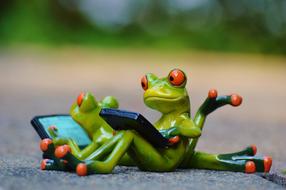 figurines of frogs with smartphones on a blurred background in the park