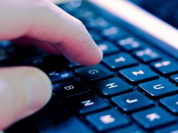 Close-up of the hand, with the shadow, typing on the keyboard of the computer