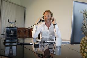 Man in white skirt, talking on the telephone, while sitting at the desk