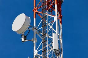 Close-up of the white and orange communication tower, at blue sky on background