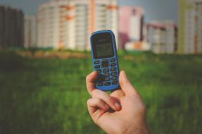 Holding blue Nokia phone in the hand at background with green grass and colorful buildings