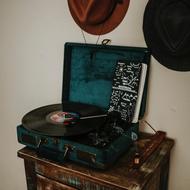 Shiny vinyl player on the table, near the wall with the colorful hats