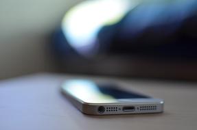 Side view of a white Iphone on a surface at blurred background