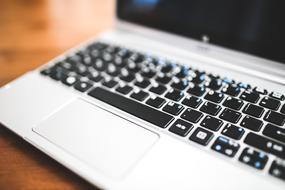 Close-up of the shiny, white and black laptop, on the wooden table, in light