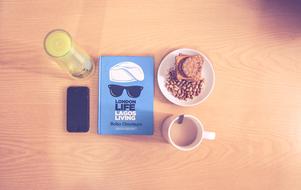 Blue, white and black book, cup of coffee, fog, smartphone and glass of juice, on the wooden table