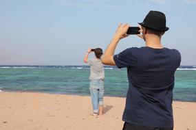 Two photographers, taking photos of a beautiful, turquoise waterscape, from the sandy beach
