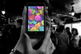 Black and white photo with the person holding smartphone with colorful smileys, among the other people