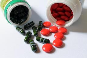 Colorful, shiny pills and tablets with containers, on the white surface, in light
