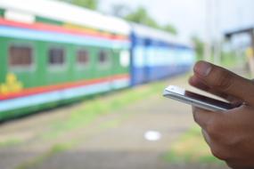 Person holding smartphone near the colorful train, among the plants