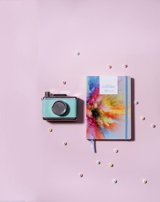 camera and colorful notepad on pink background