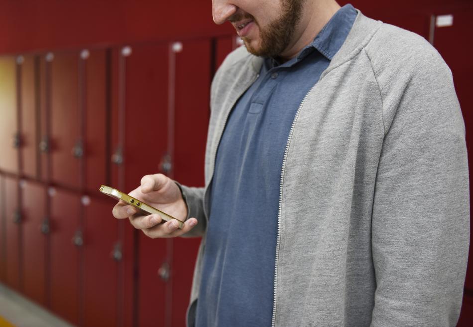 Bearded man in gray and blue clothing, using a phone, near the red lockers