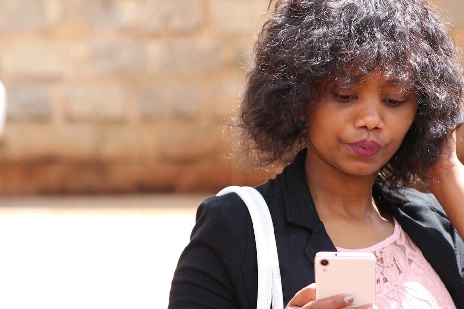 young confused woman with pink phone on blurred background